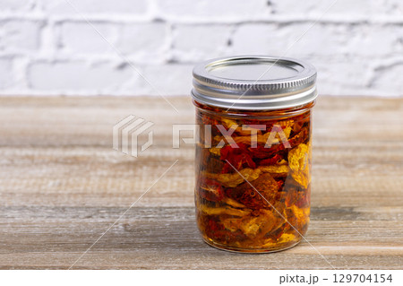 Yellow and red dried tomatoes in a jar with herbs and oil. 129704154
