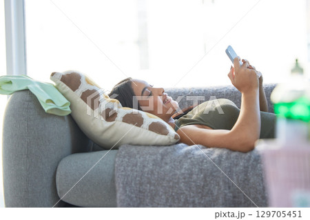Indian woman, phone and relax happy on sofa for social media, online communication and streaming video on web mobile app. Female, calm peace and relaxation or happiness watching meme on smartphone 129705451