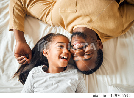 Black family, father and daughter love on a bed with a smile on face or laughing at funny memory. Above man and child together in home bedroom for bonding, support and care with safety and security 129705590