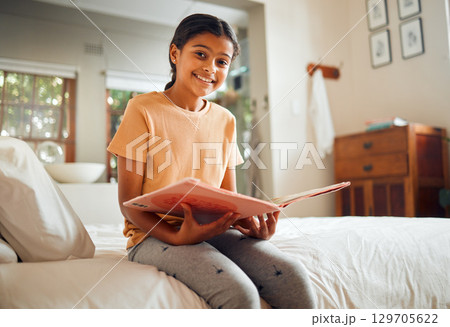 Happy little girl, reading book and bed with smile for story time, education or learning in comfort at home. Portrait of cute female child smiling in happiness holding textbook to read in the bedroom Happy little girl, reading book and bed with smile for story time, education or learning in comfort at home. Portrait of cute female child smiling in happiness holding textbook to read in the bedroom 129705622