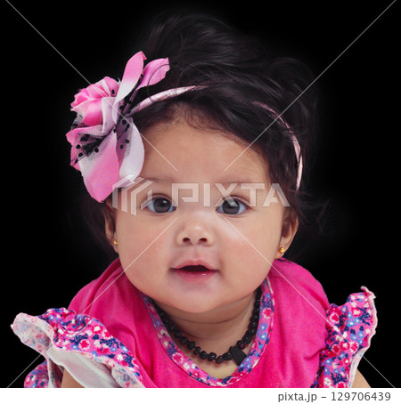 Portrait, baby or girl with an innocent infant in studio on a black background in floral clothes. Kids, flower and development with a female child on dark space for cute or adorable product placement 129706439