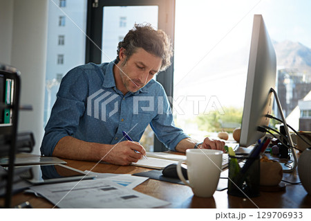 Notebook, writing and planning with a businessman working on his desk in the office for growth or development. Strategy, mindset and mission with a male employee at work to write notes in his book 129706933