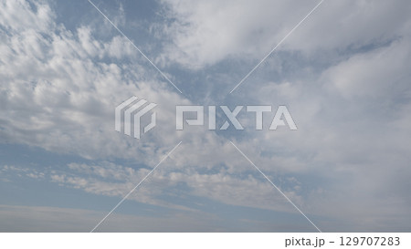 Blue sky with scattered white cirrus clouds. The clouds vary in size and shape, creating a serene atmosphere. Background light blue. 129707283