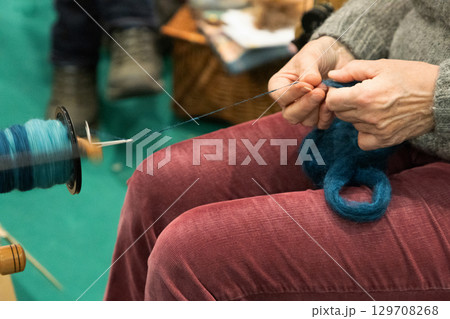 Skilled artisan spinning yarn with a spinning wheel, showcasing traditional craftsmanship and creativity Skilled artisan spinning yarn with a spinning wheel, showcasing traditional craftsmanship and creativity 129708268