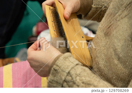 Hands of a person using a wooden carder to prepare wool fibers for spinning into yarn Hands of a person using a wooden carder to prepare wool fibers for spinning into yarn 129708269