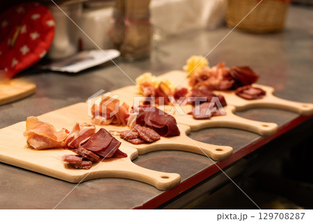 Assorted cured meats displayed on wooden boards in a rustic kitchen setting with vibrant colors Assorted cured meats displayed on wooden boards in a rustic kitchen setting with vibrant colors 129708287