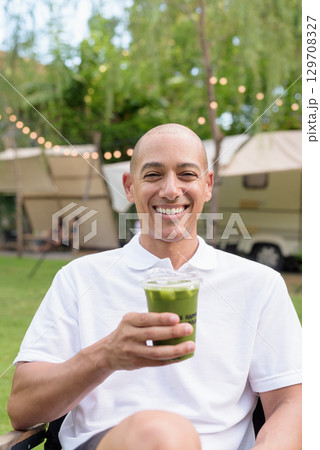 Confident bald man relaxing at campsite with camper van having healthy green detox juice drink Confident bald man relaxing at campsite with camper van having healthy green detox juice drink 129708327