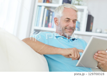 Mature man, digital tablet or relax on sofa in house, home or apartment living room on social media app or internet game. Smile, happy or retirement person on technology crossword puzzle or streaming 129708328