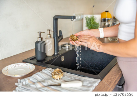 Female hands washing a fresh oyster under running tap water before opening. Hygiene and safety precautions when preparing shellfish at home. 129708556