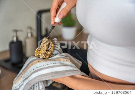 Close up view of female hands struggling to open a fresh oyster at home with a special oyster knife. Risks and challenges of handling shellfish without professional training 129708564