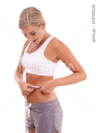 Health, fitness and woman with tape measure for abdomen in studio isolated on a white background. Diet, wellness and slim female model measuring waist to track weightloss goals, progress or targets. 129709226