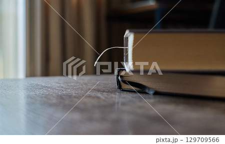 A bookmark is visible in a book resting on a wooden table indoors A bookmark is visible in a book resting on a wooden table indoors 129709566