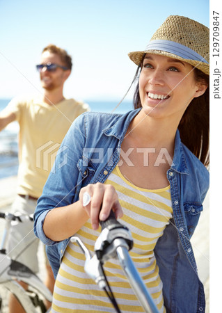 Bike, travel and couple with a woman on summer vacation or holiday riding on the promenade by the beach. Freedom, date and romance with a girlfriend outdoor for a ride on the coast during the day 129709847