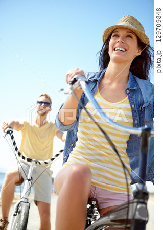 Cycling, travel and couple with a woman on summer vacation or holiday riding on the promenade by the beach. Bike, freedom and date with a girlfriend outdoor for a ride on the coast during the day 129709848