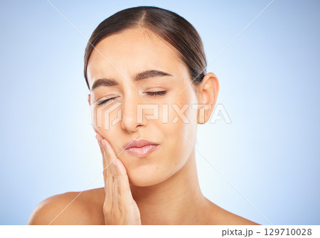 Toothache, pain and cavity with a model woman holding her mouth in studio on a blue background for oral care. Dental hygiene, plaque and face with an attractive young female rubbing her sore cheek Toothache, pain and cavity with a model woman holding her mouth in studio on a blue background for oral care. Dental hygiene, plaque and face with an attractive young female rubbing her sore cheek 129710028