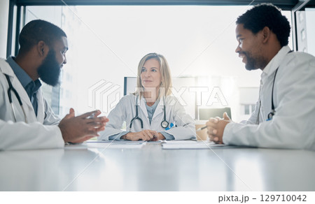 Healthcare, meeting and team of doctors talking in hospital, clinic or health care facility boardroom. Teamwork, communication and medical workers in discussion, conversation and speaking with paper 129710042