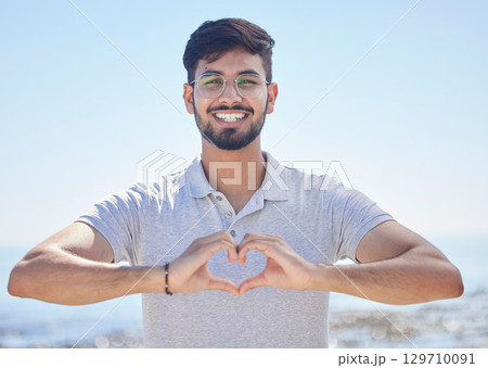 Beach portrait and a man heart hand for summer holiday freedom, happiness and wellness. Happy Indian person enjoying ocean sun with love shape and optimistic smile for travel adventure. Beach portrait and a man heart hand for summer holiday freedom, happiness and wellness. Happy Indian person enjoying ocean sun with love shape and optimistic smile for travel adventure. 129710091