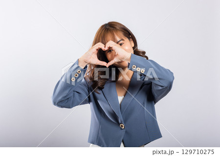 A confident business woman wear suit smiles and creates a heart symbol with two hands on white background. Asian portrait of a beautiful young female expressing love and happiness for Valentine's Day A confident business woman wear suit smiles and creates a heart symbol with two hands on white background. Asian portrait of a beautiful young female expressing love and happiness for Valentine's Day 129710275
