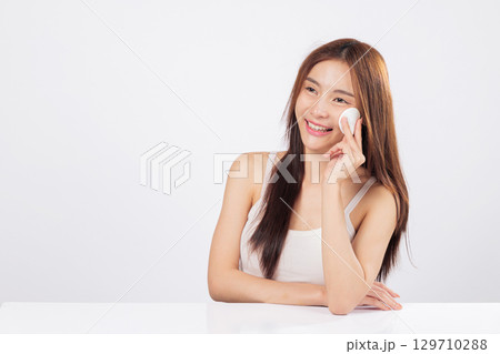 Cotton wipe and cotton pad are used by a smiling woman to clean her face, removing makeup with gentle care and a sense of skincare wellness. isolated studio white background Cotton wipe and cotton pad are used by a smiling woman to clean her face, removing makeup with gentle care and a sense of skincare wellness. isolated studio white background 129710288
