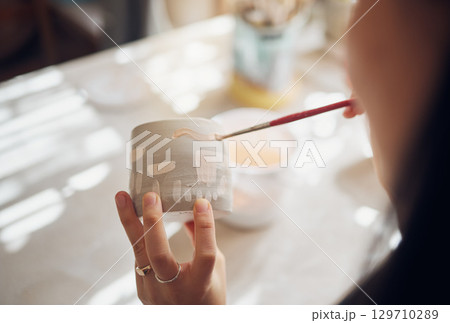 Woman hands, pottery studio and painting cup in workshop for sculpture, creative manufacturing or design. Painter, ceramics product and brush process, artistic pattern or production in small business 129710289