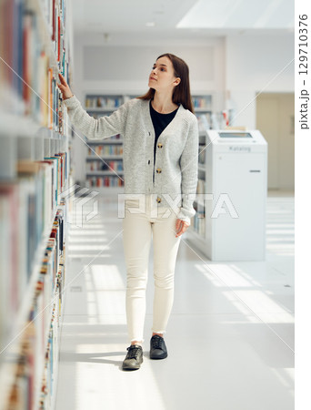 Woman, student and search in library for book choice, knowledge or learning at bookstore for education. Female looking at bookshelf in study for decision, thinking or choosing thesis for scholarship 129710376