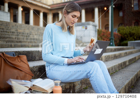 College, learning and food with woman and laptop for education, lunch break and academy research. University, knowledge and goal with girl student and sandwich on stairs of campus for relax and study 129710408