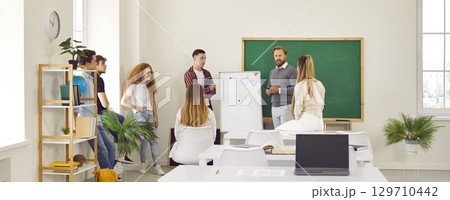 Banner with a group of students listening to their teacher standing in front of a whiteboard Banner with a group of students listening to their teacher standing in front of a whiteboard 129710442