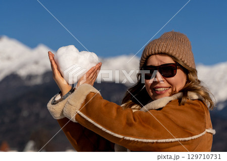 Snow Heart Mountains Winter: Woman holds snow heart, sunny mountains backdrop, joyful winter activity. 129710731