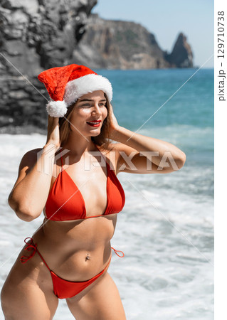 A woman in Santa hat on the seashore, dressed in a red swimsuit. New Year's celebration in a hot country 129710738