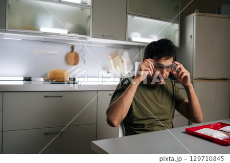 Skilled gardener male wearing safety glasses while preparing fertilizer for vertical hydroponic tower garden, ensuring safe handling of chemicals in kitchen. Concept of urban farming. 129710845