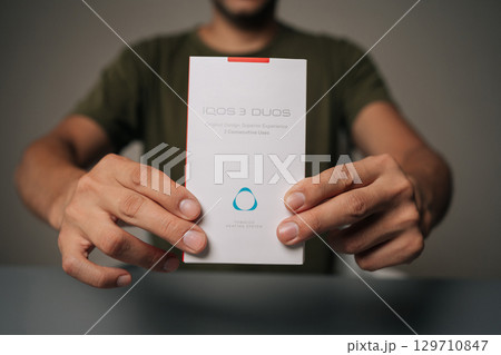 Ufa, Russia - 21 July 2025. Cropped shot of influencer male holding and presenting new IQOC 3 duos tobacco heating system, innovative electronic cigarette for modern smokers seeking harm reduction Ufa, Russia - 21 July 2025. Cropped shot of influencer male holding and presenting new IQOC 3 duos tobacco heating system, innovative electronic cigarette for modern smokers seeking harm reduction 129710847