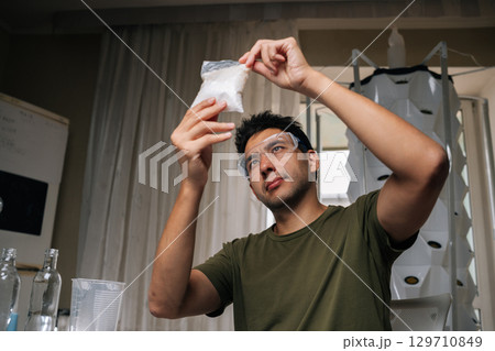 Gardening enthusiast wearing protective eyewear measuring nutrient solution for vertical hydroponic setup, maximizing plant health and productivity in compact indoor growing space 129710849