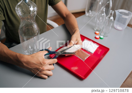 Close-up unrecognizable male hands cutting fertilizer bag, preparing nutrients for vertical hydroponic tower garden, embodying innovative urban agriculture techniques. Concept of home gardening. 129710878