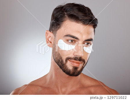 Skincare, beauty and man with mask for eyes on gray background for wellness, facial treatment and dermatology. Grooming, luxury spa and male with face patch, eye pads and cosmetics products in studio 129711022