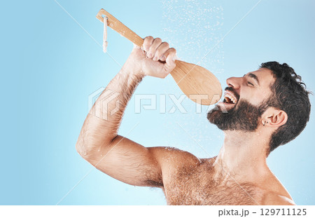 Bathroom, singing and washing with a man model in studio on a blue background using a loofah to sing. Water, showering and hygiene with a handsome male wet while cleaning for personal body care 129711125