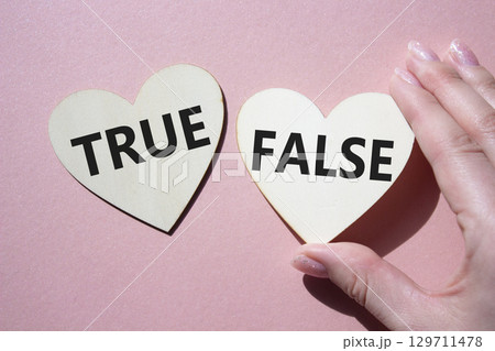 True or False symbol. Concept word True or False on wooden hearts. Businessman hand. Beautiful pink background. Business and True or False concept. Copy space 129711478