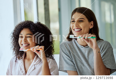Toothbrush, oral care and women friends doing a dental, health and wellness morning routine together. Happy, smile and interracial females brushing their teeth for mouth hygiene in the bathroom. Toothbrush, oral care and women friends doing a dental, health and wellness morning routine together. Happy, smile and interracial females brushing their teeth for mouth hygiene in the bathroom. 129711698