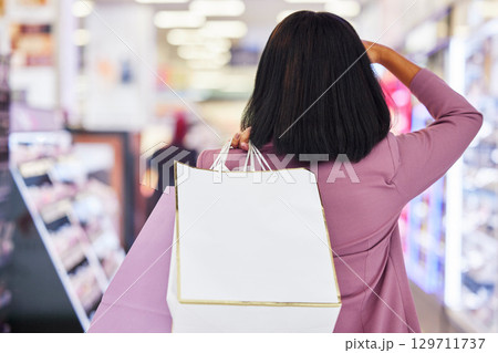 Woman, shopping and window display in a mall for retail. therapy, sale and customer discount at a store. Paper bag, fashion and female looking at clothes or makeup on promotion on commerce travel 129711737