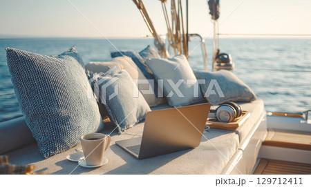 A serene scene on a yacht deck featuring a laptop, headphones, and a cup of coffee, set against the calm blue sea, symbolizing remote work, luxury travel, and a balanced digital nomad lifestyle 129712411