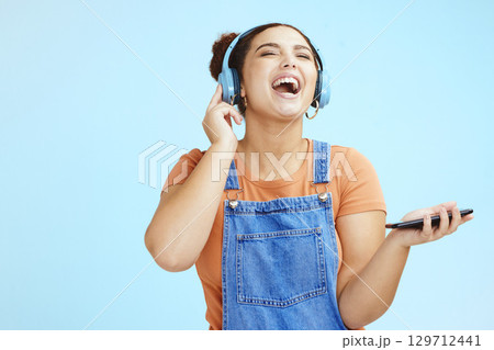 Mockup, headphones and woman with smartphone, happy or connection on blue studio background. Fun, female or girl laughing, cellphone for music or headset for podcast, online streaming or social media 129712441