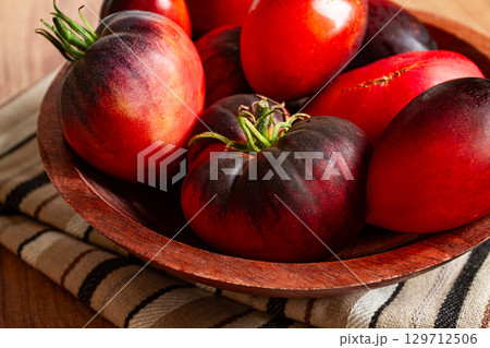 Freshly picked tomatoes, of the Black Beauty variety, in a wooden bowl, close-up, on the kitchen table, Freshly picked tomatoes, of the Black Beauty variety, in a wooden bowl, close-up, on the kitchen table, 129712506