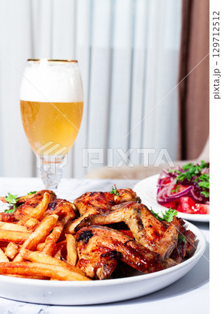Delicious barbecue chicken wings, with French fries, salad and a refreshing drink, at a cozy table, there are no people Delicious barbecue chicken wings, with French fries, salad and a refreshing drink, at a cozy table, there are no people 129712512