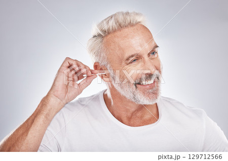Elderly man, ear cleaning with cotton swab for hygiene, grooming and clean body with cosmetic care against studio background. Beauty, health and wellness, senior male and happy with natural cosmetics Elderly man, ear cleaning with cotton swab for hygiene, grooming and clean body with cosmetic care against studio background. Beauty, health and wellness, senior male and happy with natural cosmetics 129712566