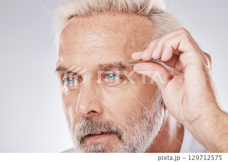 Beauty, eyebrows and senior man with tweezers for facial hair grooming, shaping and cosmetic care on a studio background. Hair removal, clean and face of a model with a tool for trimming brows 129712575