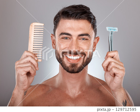 Portrait, shaving and comb with a man model holding a razor in studio on a gray background for skincare. Face, wellness and hands with a handsome young male in the bathroom to shave his beard Portrait, shaving and comb with a man model holding a razor in studio on a gray background for skincare. Face, wellness and hands with a handsome young male in the bathroom to shave his beard 129712595