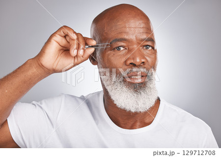 Senior black man, eyebrow and tweezer for self care and grooming for clean, glow and fresh skin and face. Portrait of African male for facial hair removal or epilation on grey studio background 129712708