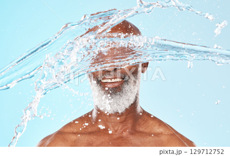 Happy black man, face and water splash in studio for cleaning, self care and headshot cosmetics on blue background. Shower, wellness and male beauty with water drops, healthy skincare and facial body 129712752