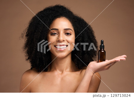 Face portrait, skincare and black woman with bottle in studio isolated on a brown background. Makeup, cosmetics and female model holding hyaluronic acid, product or essential oil for facial treatment 129713024