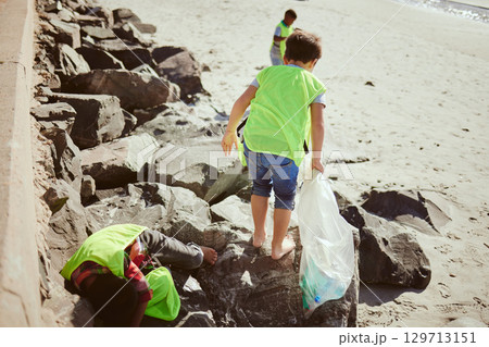 Environment, cleaning and children with dirt on beach for clean up, pollution and eco friendly volunteer. Sustainability, recycle and kids reduce waste, pick up trash and plastic bag on beach sand 129713151