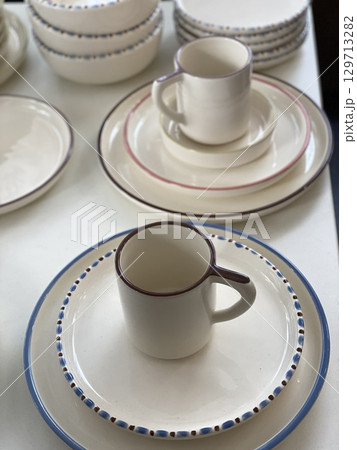 Ceramic dishes and mugs stacked on a white table as a decorative kitchen background Ceramic dishes and mugs stacked on a white table as a decorative kitchen background 129713282